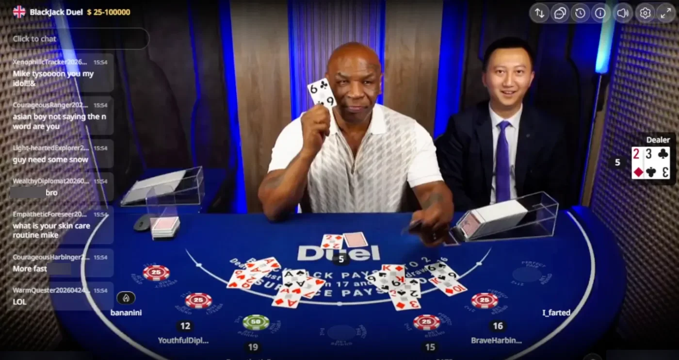 Mike Tyson holding up a six of clubs at the Duel Blackjack Live table, with a dealer in a dark suit beside him and the stream chat on the left